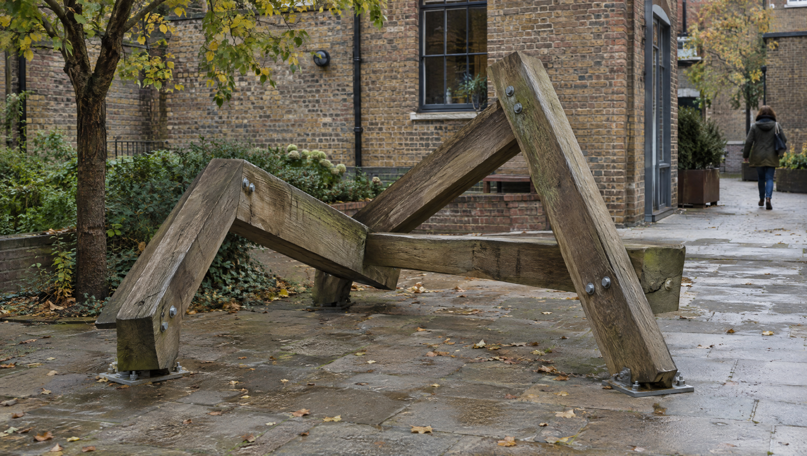 Invented low sculpture of reclaimed oak beams with visible bolts in a brick courtyard